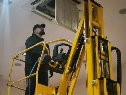 Technicien en intervention sur une unité de climatisation en hauteur